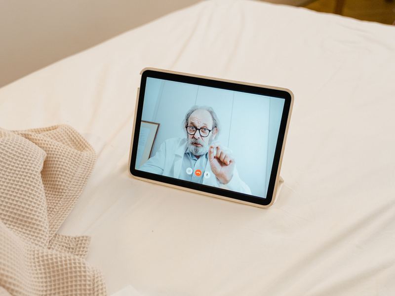 A telehealth video visit with a provider on a tablet propped on a bed.
